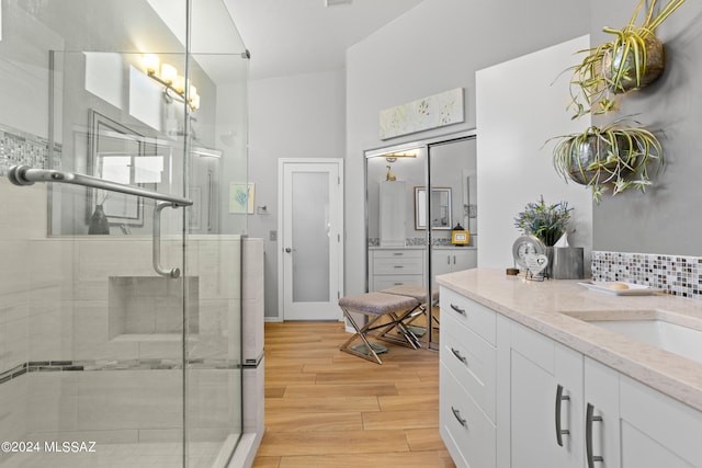 bathroom with vanity, hardwood / wood-style flooring, tasteful backsplash, and a shower with door