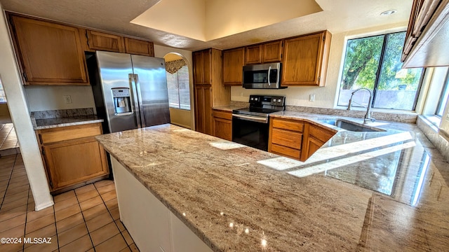 kitchen with light stone counters, light tile patterned floors, stainless steel appliances, and sink