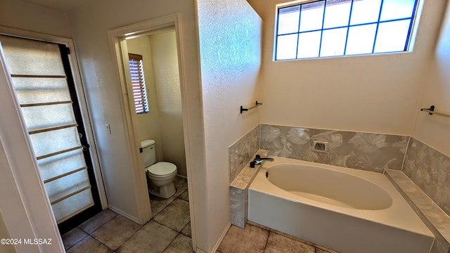 bathroom featuring tile patterned flooring, a bath, and toilet