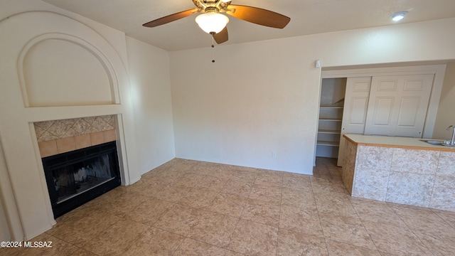 unfurnished living room featuring ceiling fan, sink, and a tile fireplace