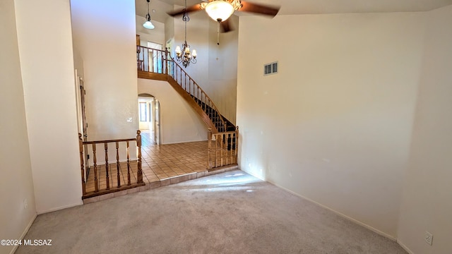 unfurnished living room with ceiling fan with notable chandelier, a high ceiling, and carpet