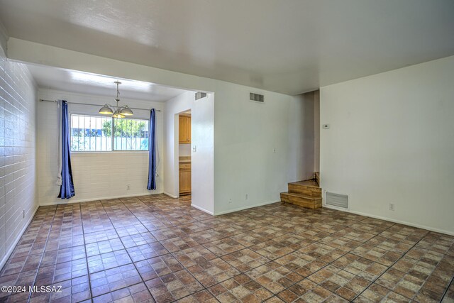 spare room featuring an inviting chandelier and brick wall