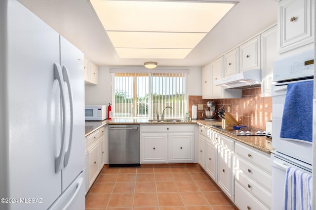 kitchen featuring white appliances, white cabinets, decorative backsplash, under cabinet range hood, and a sink