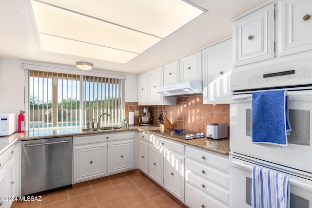 kitchen featuring under cabinet range hood, white appliances, a sink, white cabinets, and decorative backsplash