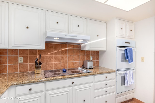 kitchen with electric cooktop, double oven, tasteful backsplash, light stone counters, and white cabinetry