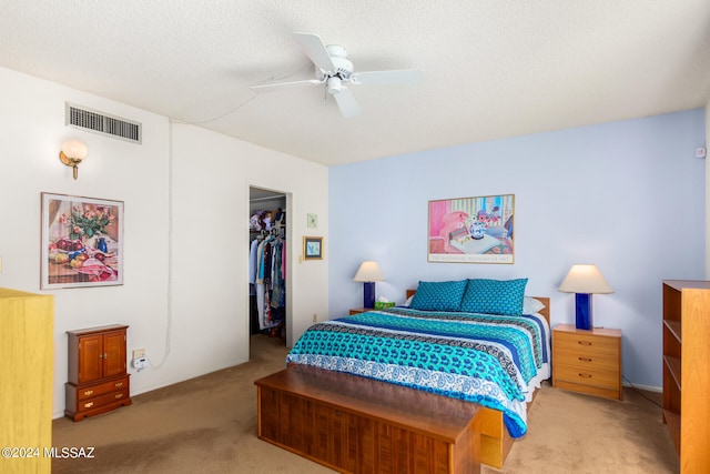 bedroom featuring a textured ceiling, light colored carpet, ceiling fan, a spacious closet, and a closet