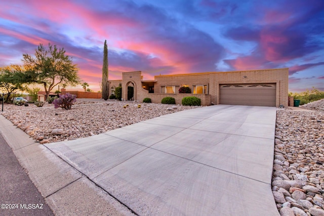 pueblo-style house with concrete driveway, brick siding, and an attached garage