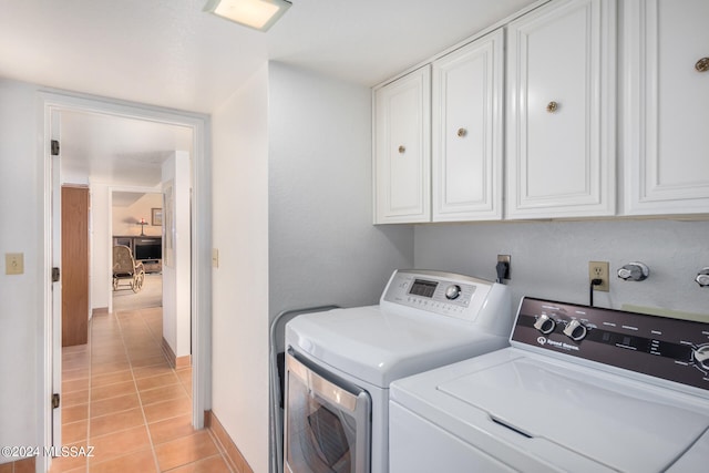 clothes washing area featuring light tile patterned floors, washer and clothes dryer, cabinet space, and baseboards