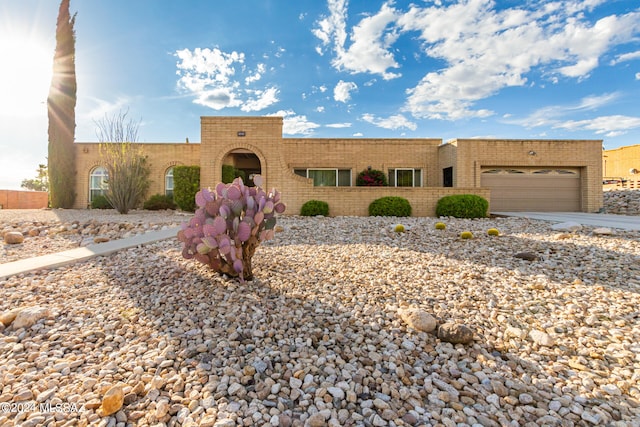 pueblo-style house featuring driveway, brick siding, and an attached garage