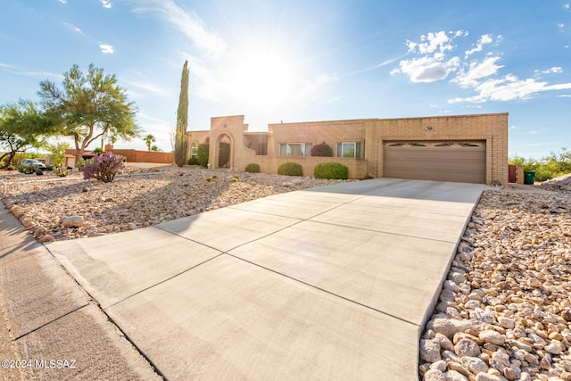 pueblo-style home featuring a garage, brick siding, and driveway