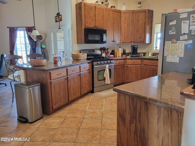 kitchen with light tile patterned floors, kitchen peninsula, decorative light fixtures, stainless steel appliances, and a towering ceiling