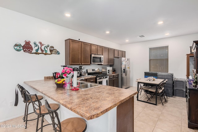 kitchen with kitchen peninsula, a breakfast bar, dark brown cabinetry, light tile patterned floors, and appliances with stainless steel finishes