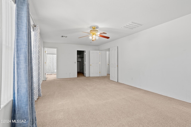 unfurnished bedroom with connected bathroom, ceiling fan, light carpet, and a walk in closet