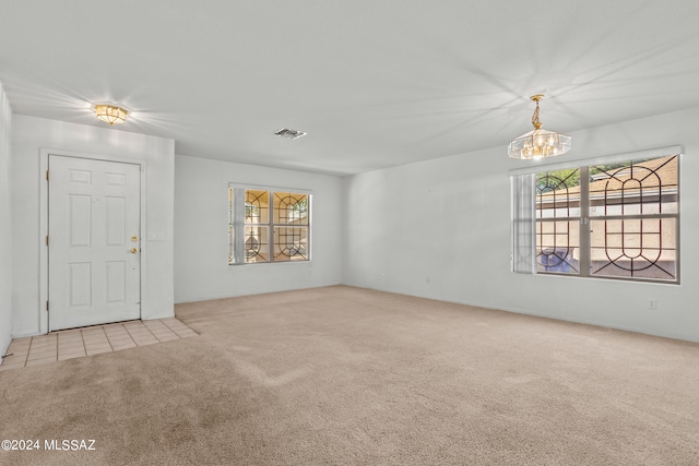 unfurnished room featuring light carpet and an inviting chandelier