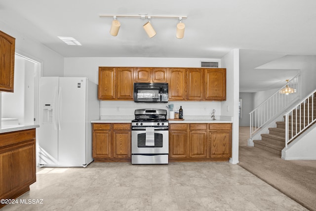 kitchen with white fridge with ice dispenser, gas range, light colored carpet, rail lighting, and a chandelier