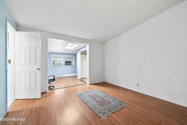 unfurnished room with light hardwood / wood-style floors, vaulted ceiling with skylight, and brick wall