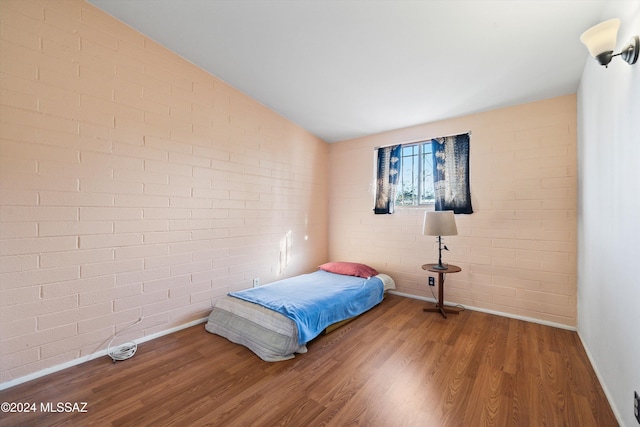 bedroom featuring hardwood / wood-style flooring, brick wall, and vaulted ceiling