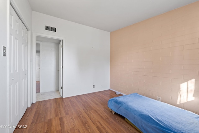 bedroom with a closet, brick wall, and light wood-type flooring