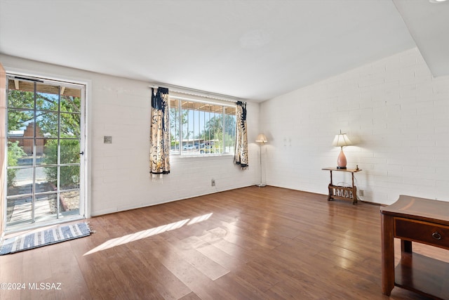 interior space with hardwood / wood-style flooring, lofted ceiling, and brick wall