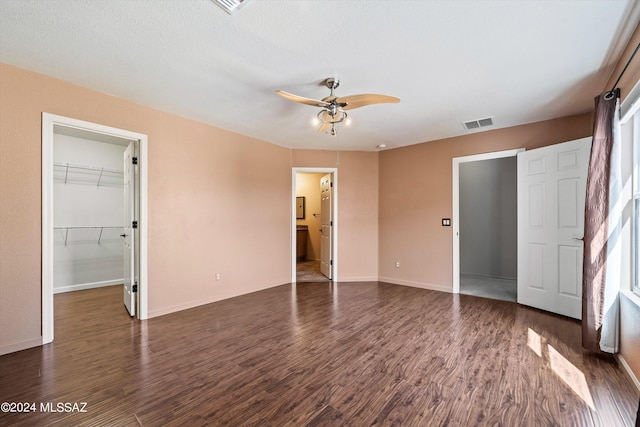 unfurnished bedroom featuring a closet, a spacious closet, dark hardwood / wood-style flooring, ensuite bathroom, and ceiling fan