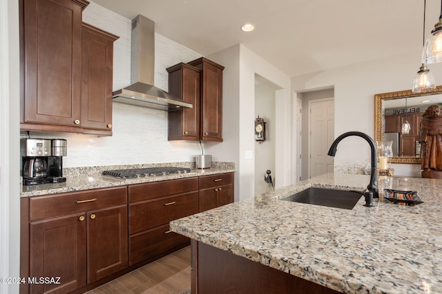 kitchen with light stone countertops, wall chimney exhaust hood, stainless steel gas cooktop, sink, and decorative light fixtures