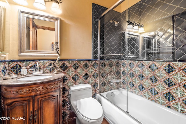 full bathroom with tile walls, vanity, combined bath / shower with glass door, and toilet