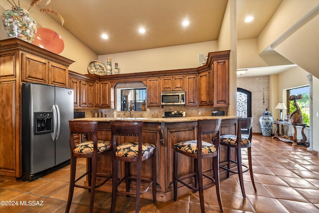 kitchen with appliances with stainless steel finishes, sink, a kitchen breakfast bar, high vaulted ceiling, and decorative backsplash