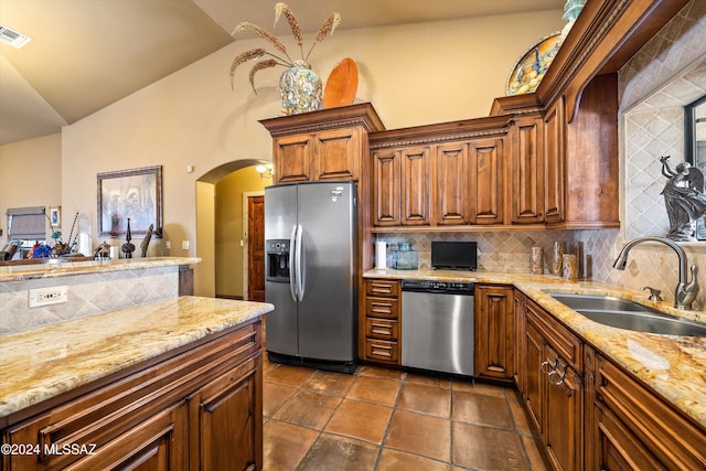 kitchen featuring stainless steel appliances, backsplash, sink, vaulted ceiling, and light stone counters