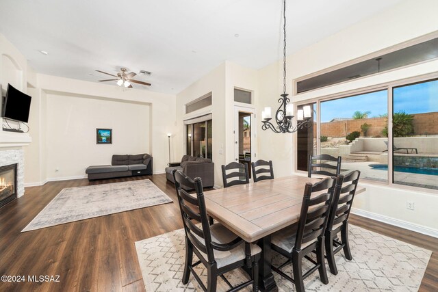 dining space featuring a fireplace, dark hardwood / wood-style flooring, and ceiling fan with notable chandelier