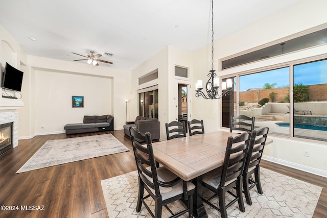 1220 W Calabria Ct, Tucson, AZ 85755 - dining space featuring a glass covered fireplace, dark wood-type flooring, a chandelier, ceiling fan, and baseboards