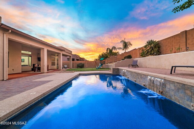 pool at dusk featuring a patio and pool water feature