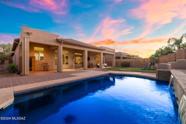 pool at dusk with a playground, pool water feature, and a patio area