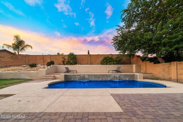 pool at dusk with a patio and pool water feature