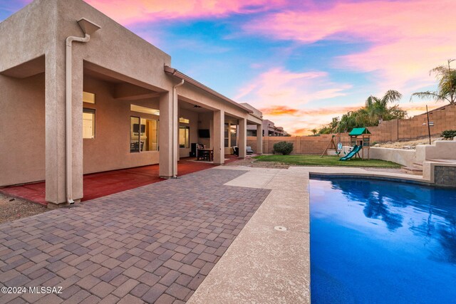 pool at dusk with a patio area and a playground