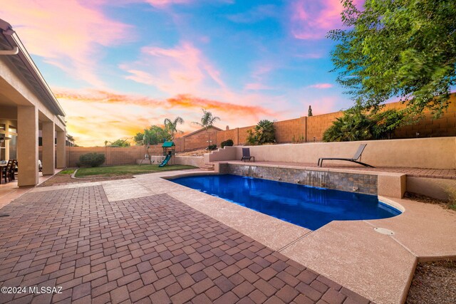 pool at dusk featuring a patio and pool water feature