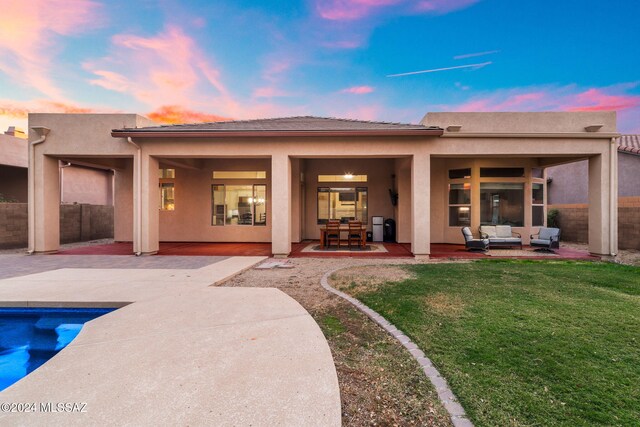 back house at dusk with an outdoor living space, a lawn, and a patio area