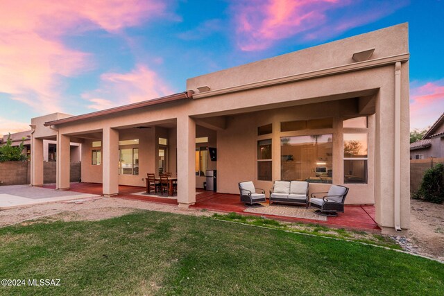 back house at dusk featuring a lawn, outdoor lounge area, and a patio