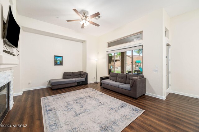 living room featuring dark wood-type flooring, ceiling fan, and a fireplace