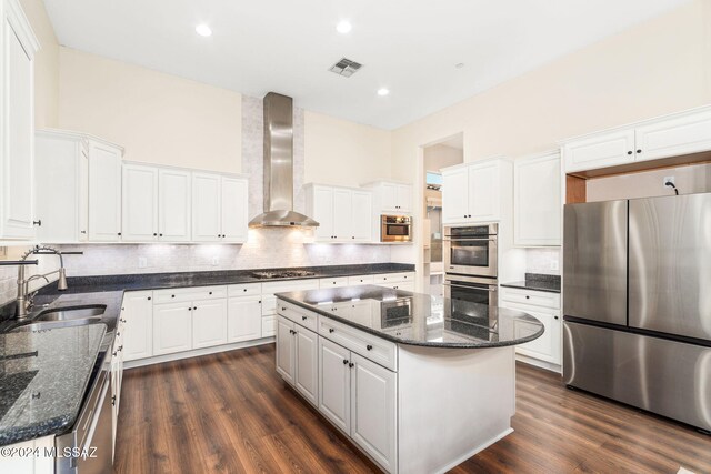 kitchen featuring stainless steel appliances, a kitchen island, wall chimney range hood, sink, and white cabinets