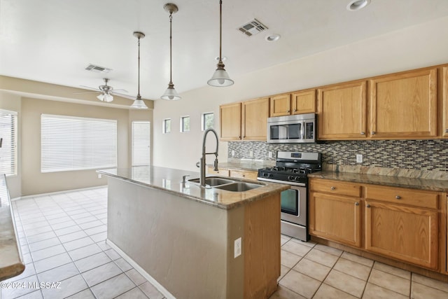 kitchen featuring stainless steel appliances, ceiling fan, sink, decorative light fixtures, and an island with sink