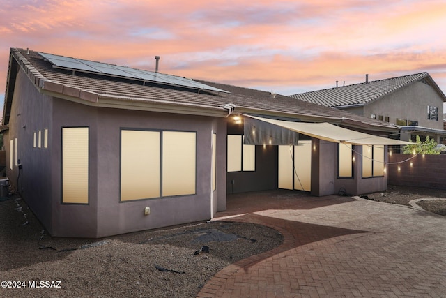 back house at dusk featuring solar panels, cooling unit, and a patio area