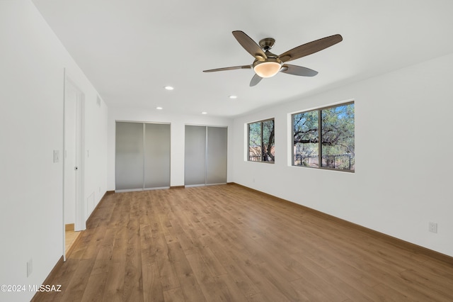 unfurnished bedroom featuring ceiling fan, light hardwood / wood-style floors, and multiple closets