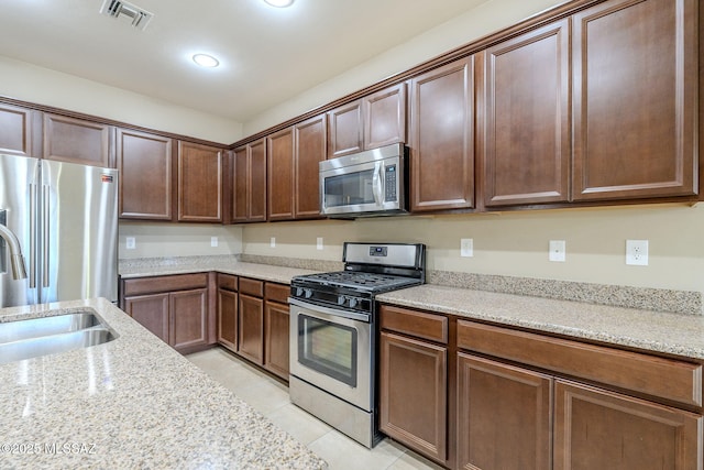 kitchen with sink, light stone countertops, stainless steel appliances, and light tile patterned floors