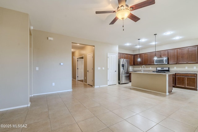 kitchen with appliances with stainless steel finishes, a kitchen island with sink, sink, light tile patterned floors, and decorative light fixtures