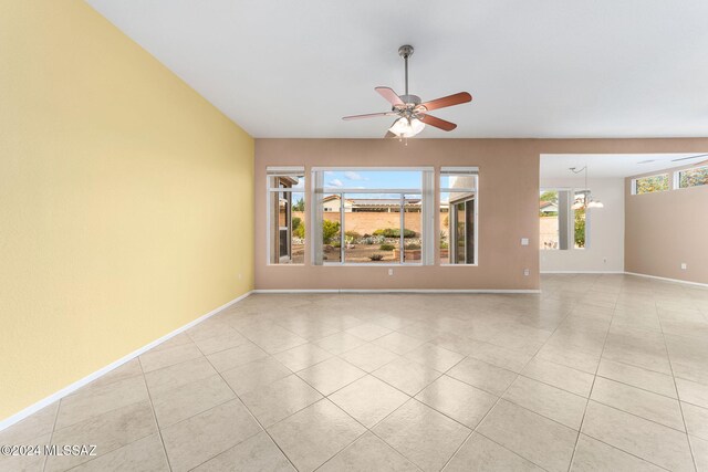 tiled spare room featuring ceiling fan with notable chandelier