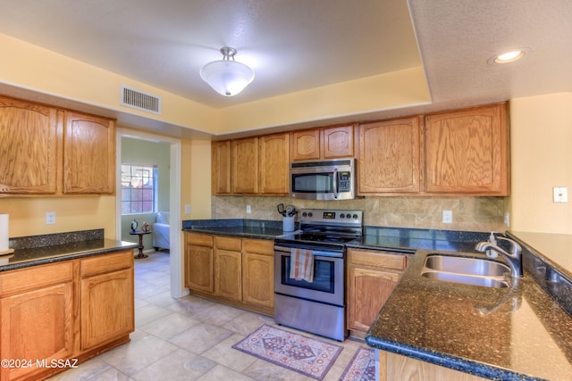 kitchen with stainless steel appliances, tasteful backsplash, sink, and dark stone counters