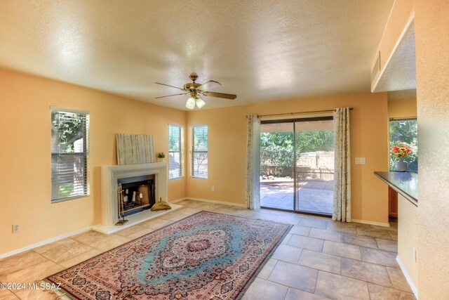 10081 N Pitchingwedge Ln, Tucson, AZ 85737 - unfurnished living room featuring ceiling fan, a fireplace with raised hearth, a textured ceiling, baseboards, and light tile patterned floors