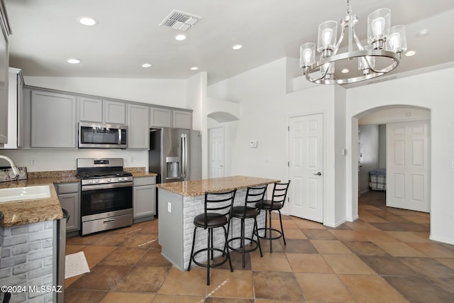 kitchen featuring appliances with stainless steel finishes, sink, a center island, gray cabinetry, and decorative light fixtures