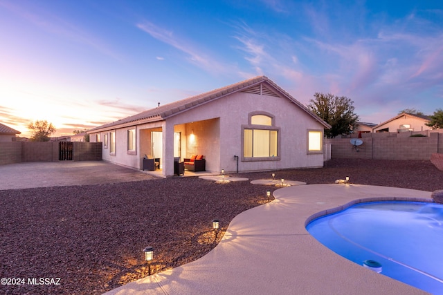 back house at dusk featuring a fenced in pool and a patio area