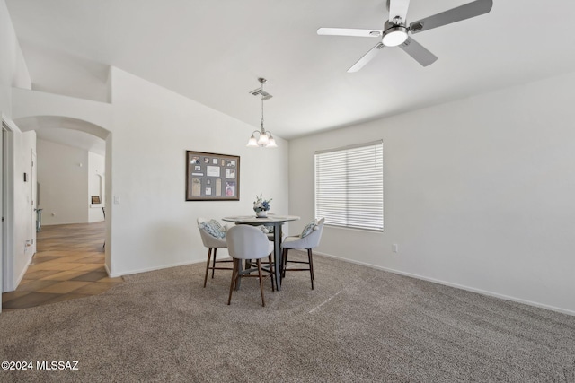 carpeted dining room with ceiling fan with notable chandelier and vaulted ceiling